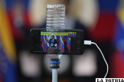 La imagen del líder de la oposición venezolana Juan Guaidó se ve en la pantalla de un teléfono celular dentro de una botella de plástico que lo sostiene firme /Foto AP /Ariana Cubillos