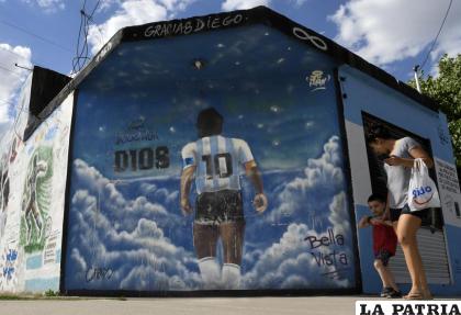 Una mujer y un niño pasan caminando frente a un mural que muestra a Diego Mardona de espaldas en el barrio Lomas de Marilo /AP Photo /Gustavo Garello