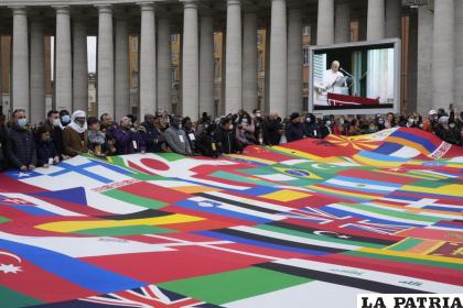 Miembros de una asociación de migrantes sostienen un letrero enorme hecho con varias banderas mientras el papa Francisco pronuncia la oración del Angelus /AP Foto/Gregorio Borgia
