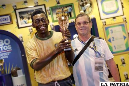 Un hincha argentino tomándose una foto con el monumento de Pelé
