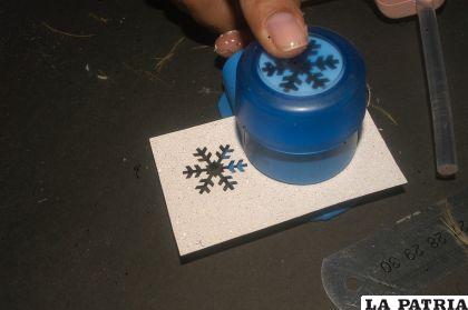 PASO 8
Perforar la goma Eva glitter blanco y celeste en forma de copos de nieve y pegar éstos en la tarjeta para decorar.
