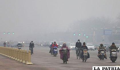 Motoristas usan mascarillas para protegerse de la contaminación, mientras circulan por una calle de Pekín