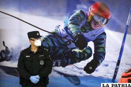 Un agente de policía con mascarilla y gafas protectoras ante un cartel con la imagen de una esquiadora /AP Foto /Mark Schiefelbein, Archivo