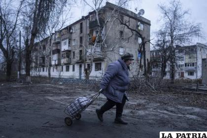 Una mujer camina a un centro de distribución de ayuda humanitaria frente a una vivienda dañada por los ataques rusos /AP Foto /Evgeniy Maloletka